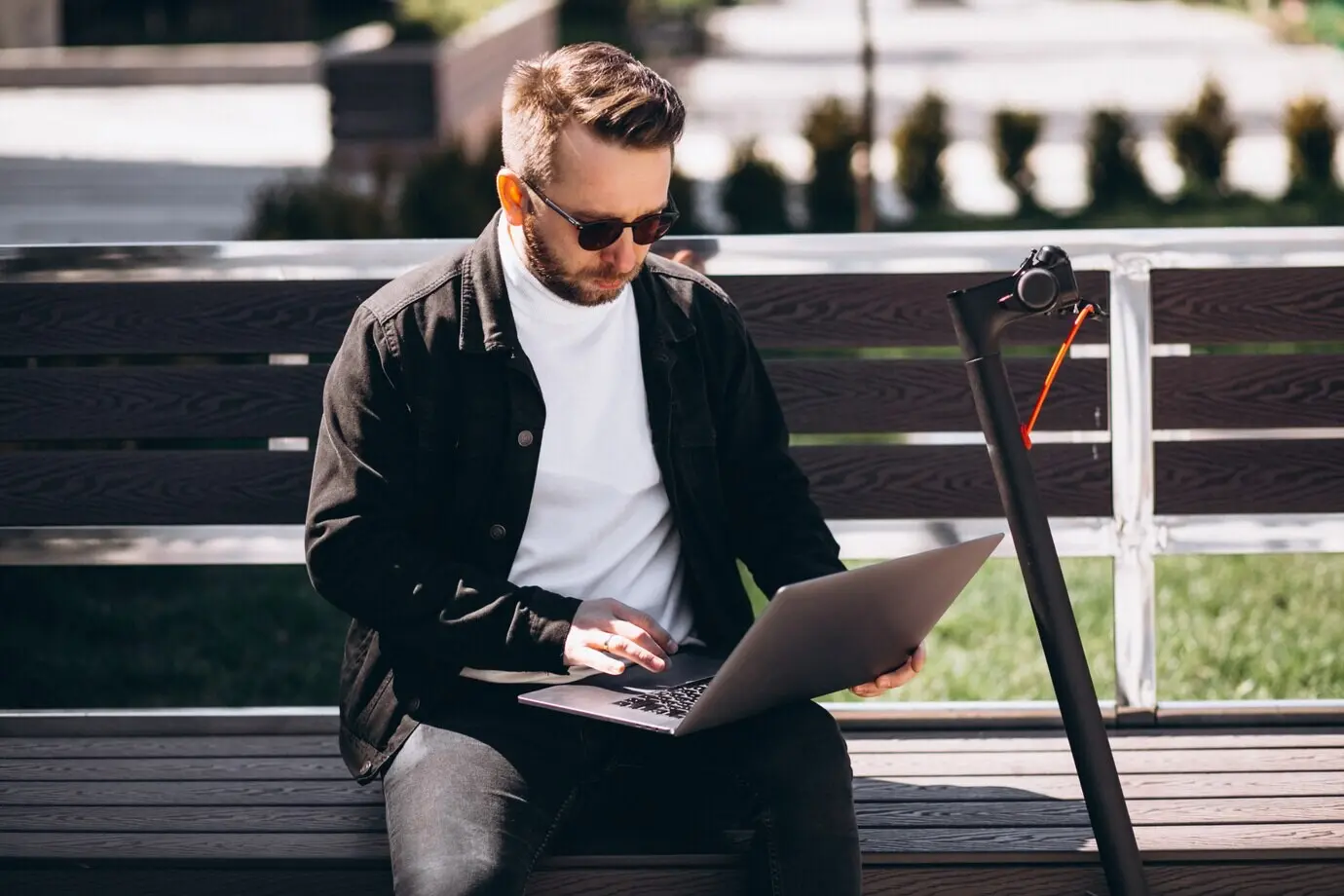 A young businessman is sitting on the bench and working on a computer.