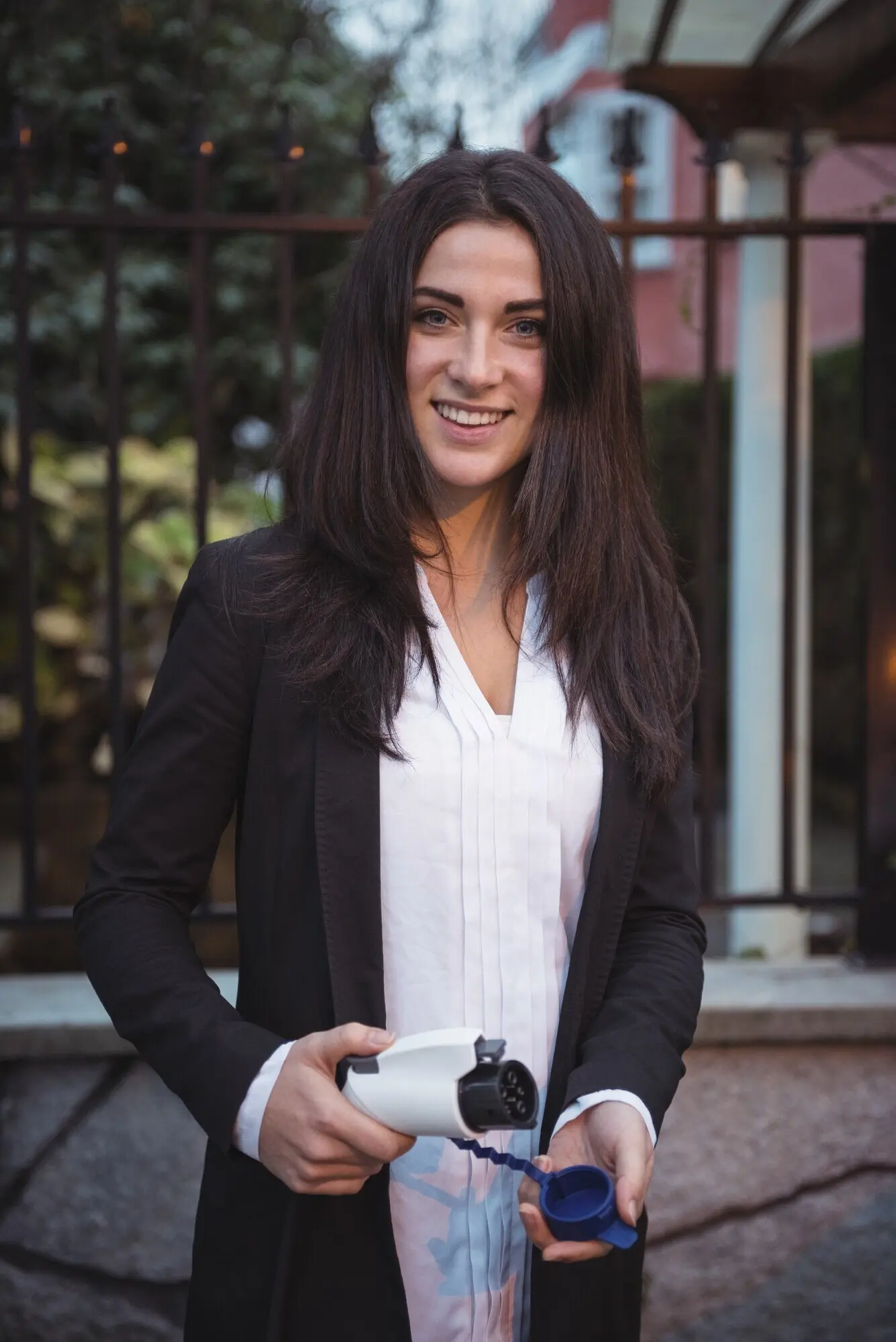 A woman smiles while holding a car charger at an electric vehicle charging station.